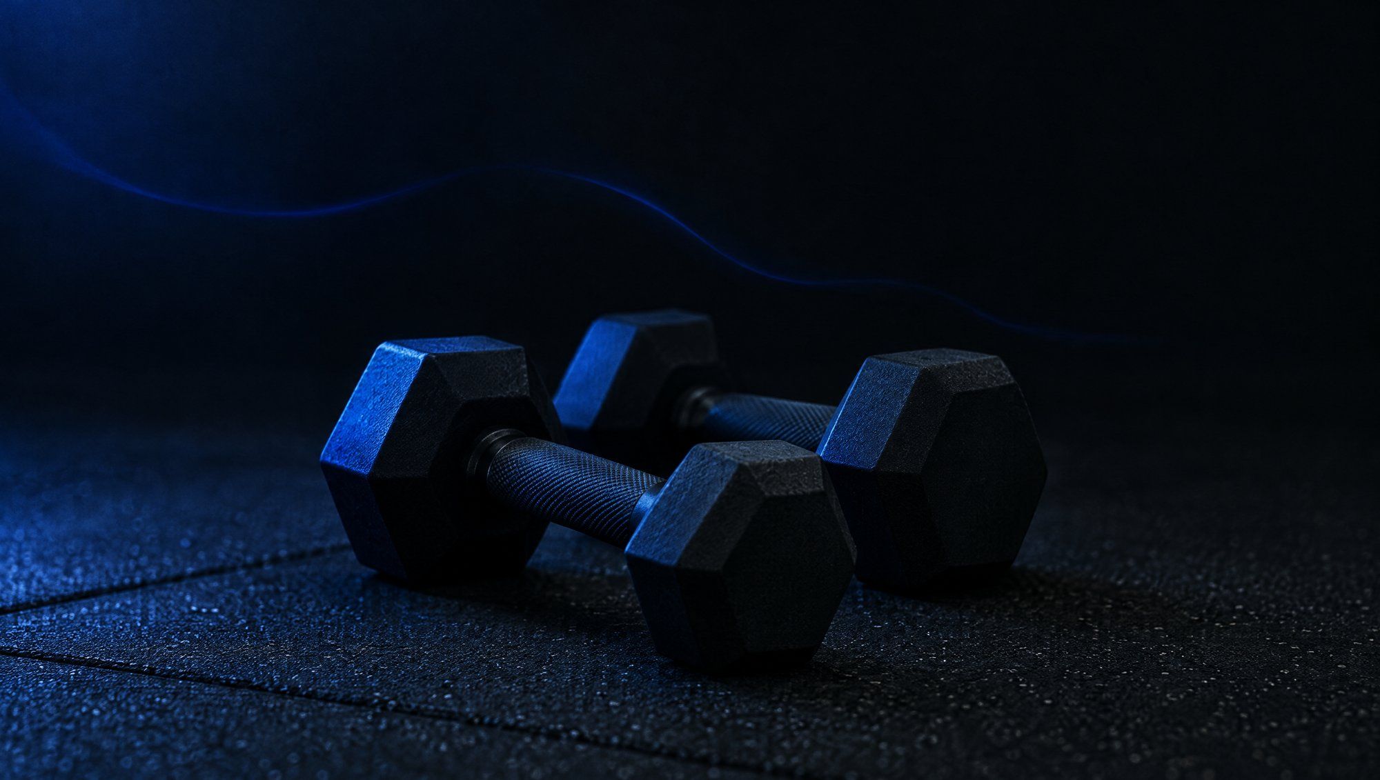 A pair of black hexagonal dumbbells on a dark rubber gym floor, with a faint thread of blue light drifting above them.
