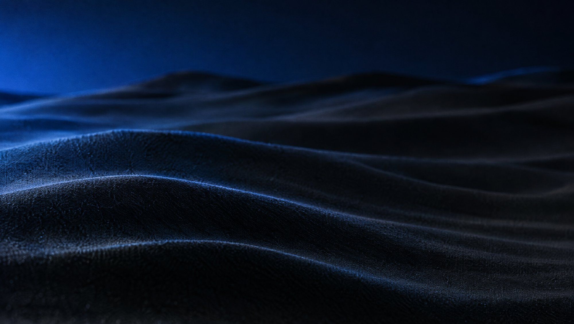 Rippled sand dunes at dusk with deep shadows in the troughs and a cool blue glow along the ridges.