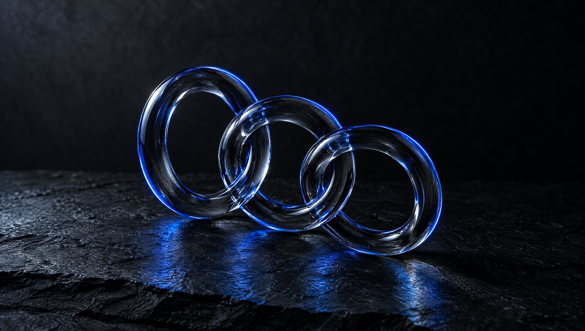 Three interlocking rings of clear glass standing on dark slate, each edged in navy-blue light, with blue reflections on the stone.