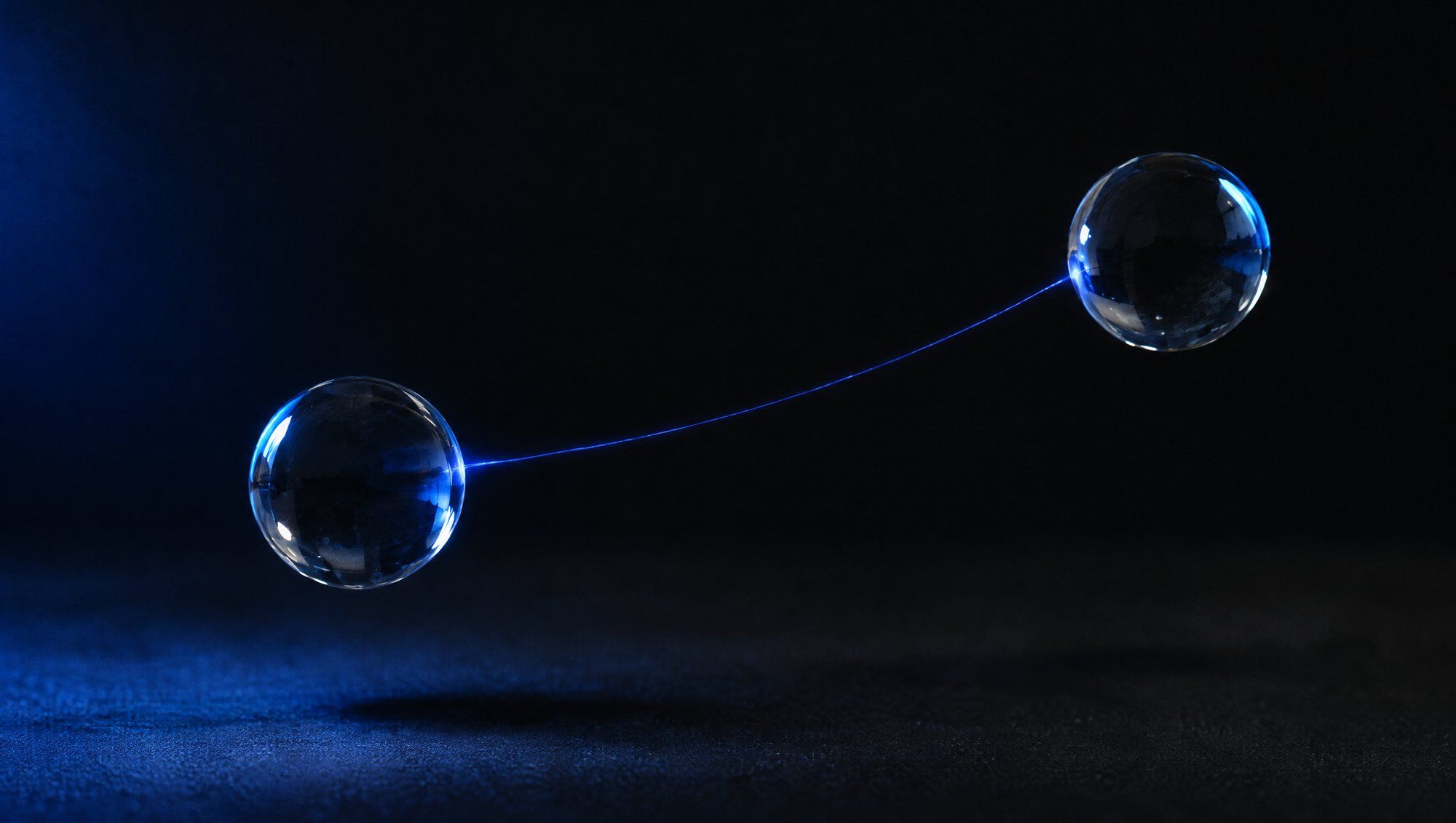 Two clear glass spheres floating apart in darkness, joined by a single thin thread of blue light.